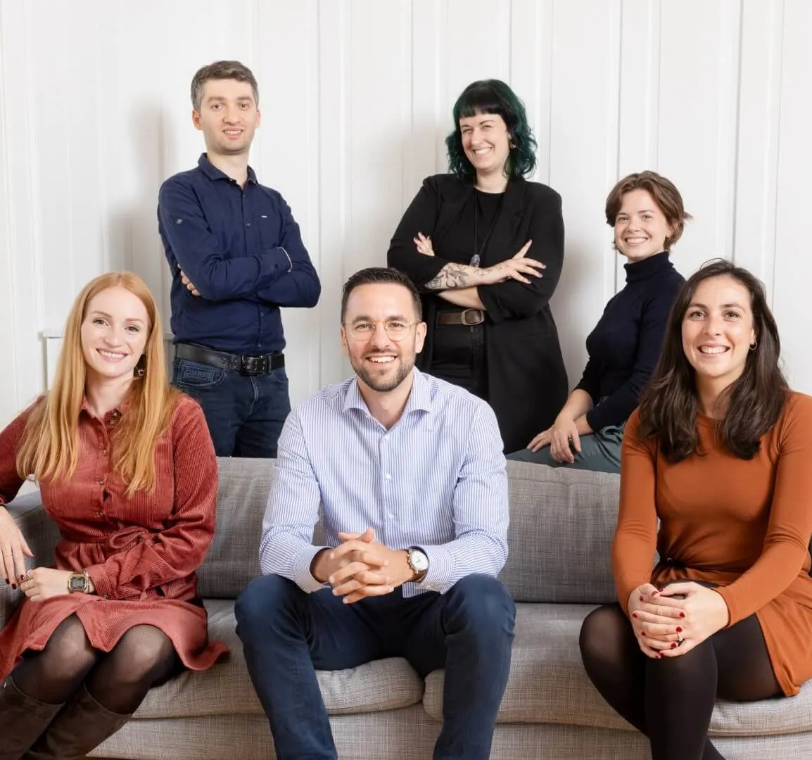 Six Eturnity team members smiling together on and around a sofa in a bright office