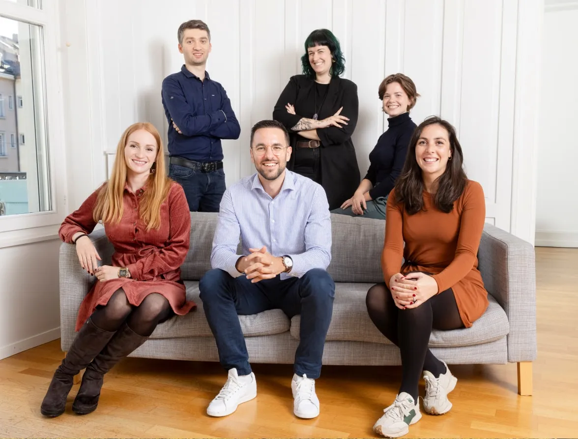 Six Eturnity team members smiling together on and around a sofa in a bright office
