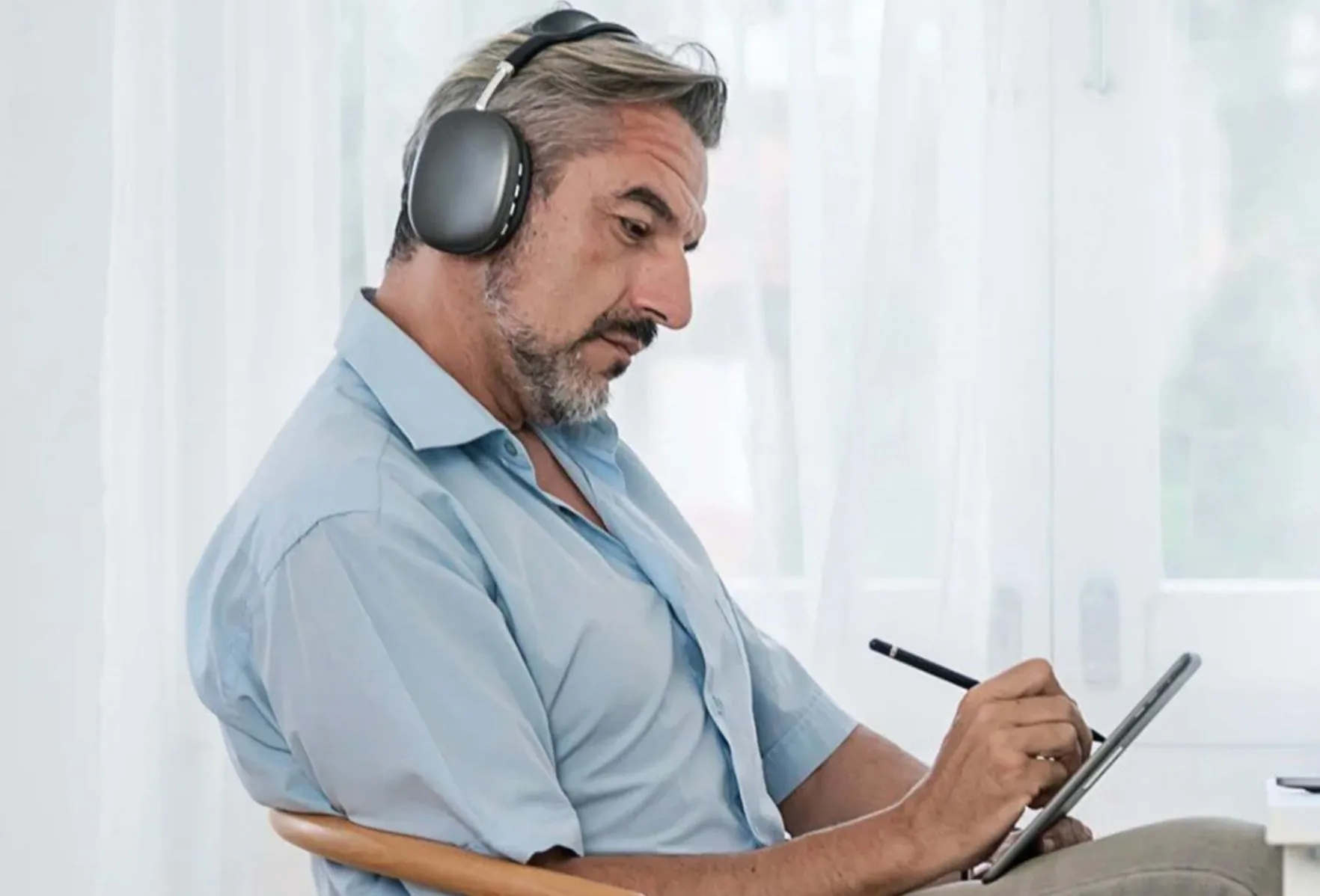 A man wearing headphones writing on a tablet with a stylus while watching a training session