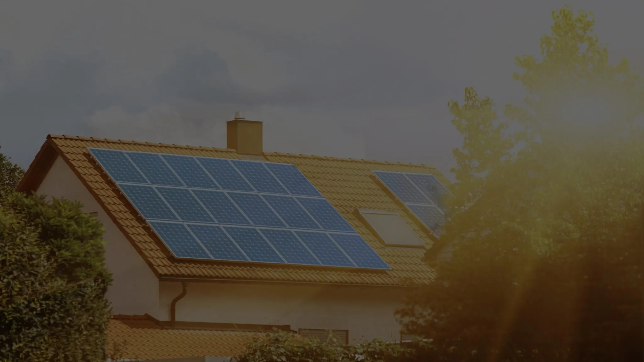 A house with solar panels on its tiled roof, trees lit by evening sun