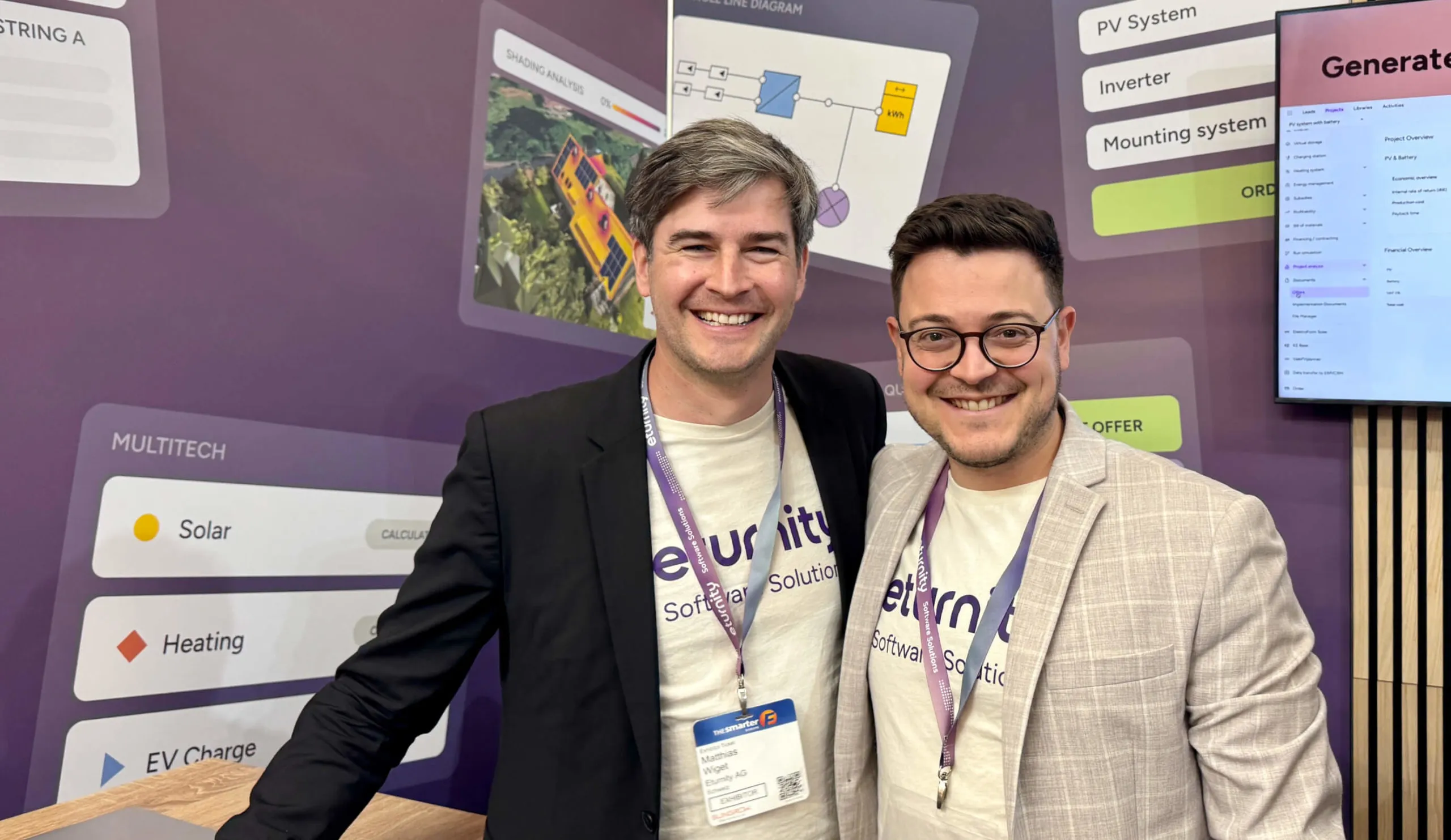 Zwei lachende Männer in Eturnity-Shirts vor der Messewand mit Motiven aus der Software
