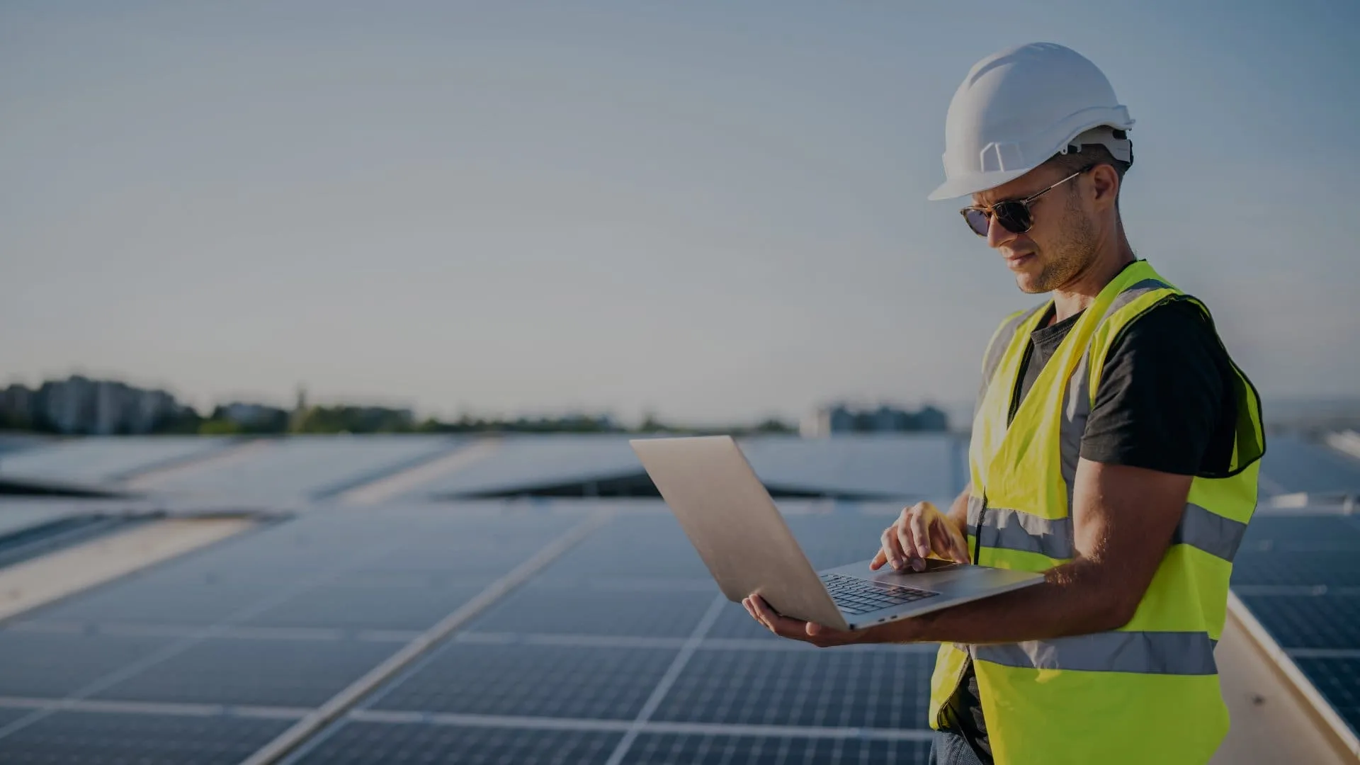 Un installateur en casque et gilet de sécurité travaille sur son ordinateur portable, au milieu d’une grande toiture couverte de panneaux solaires