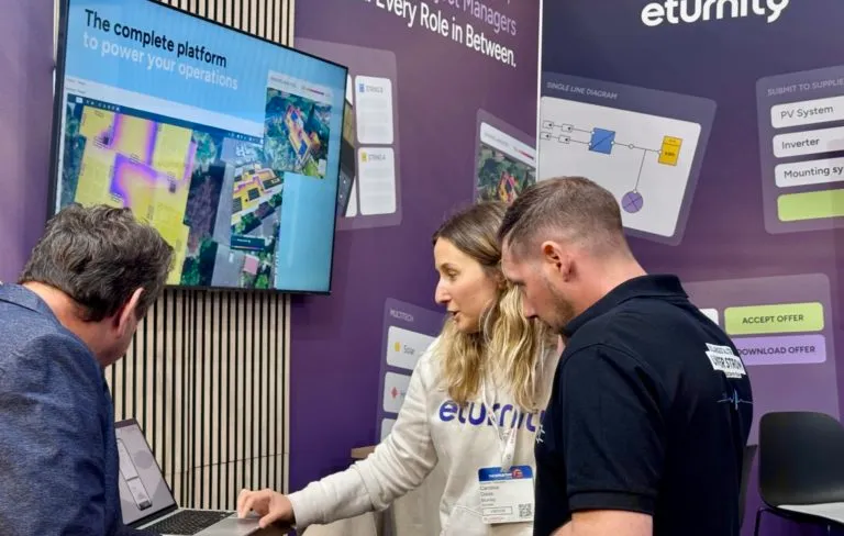 Eine Eturnity-Mitarbeiterin zeigt zwei Besuchern am Messestand die Software auf einem Laptop