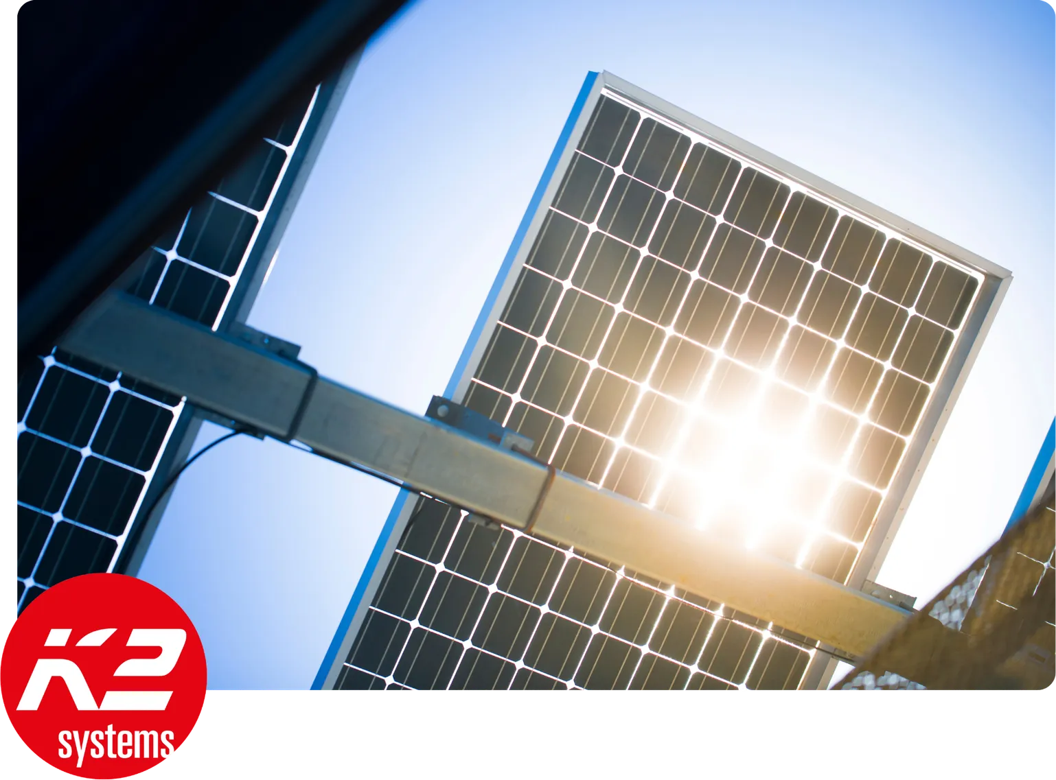 Raggi di sole dietro ai moduli solari fissati da guide di montaggio in alluminio, con il logo rosso K2 systems nell'angolo