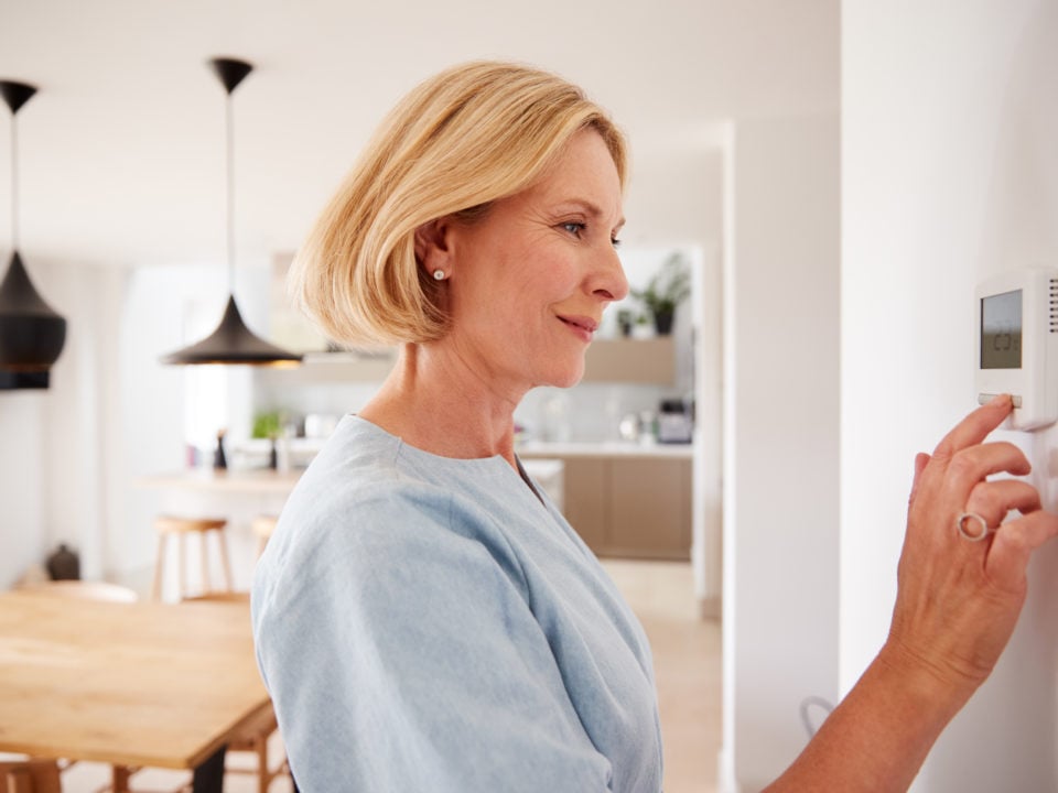 Close Up Of Mature Woman Adjusting Central Heating Temperature At Home On Thermostat